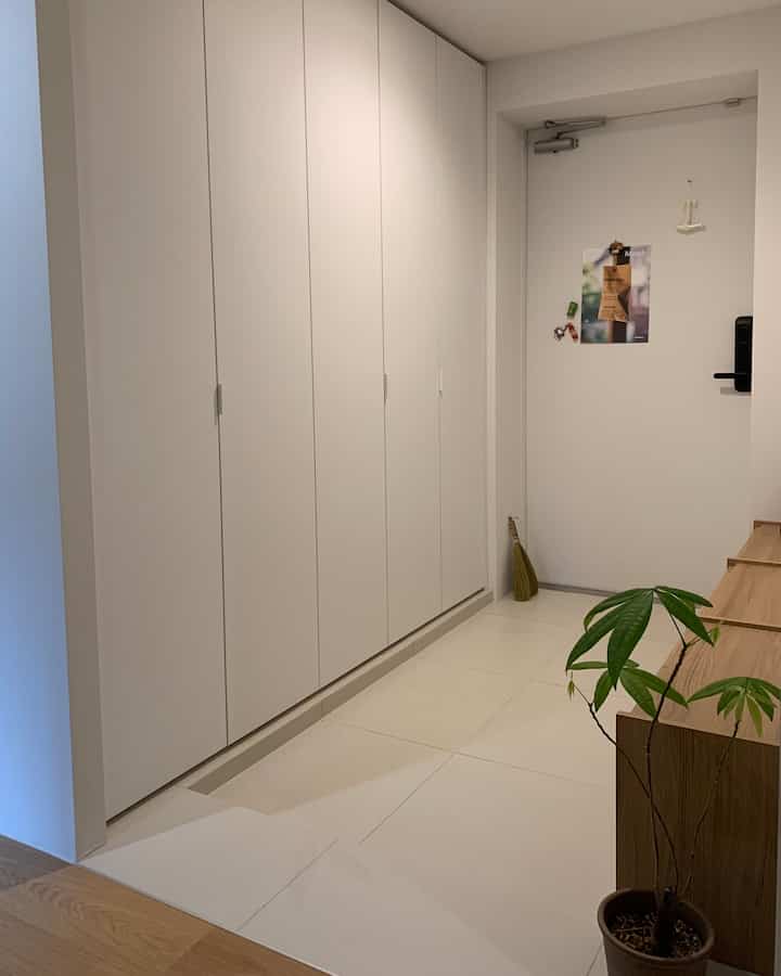 白と茶色のトーンの玄関、大型のシューズラックが壁一面を占めて清潔感のある雰囲気の空間