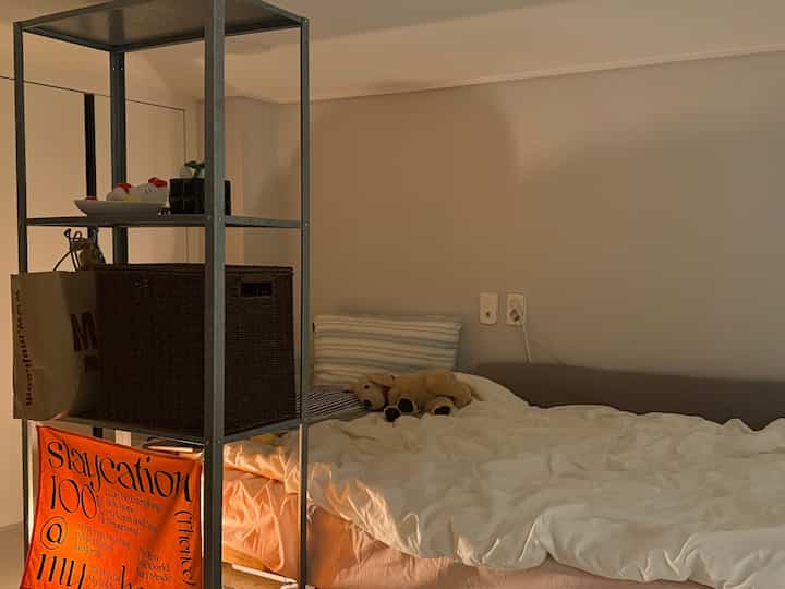 ベージュ色の壁と白い寝具がある寝室、棚と犬のぬいぐるみが温かみのある雰囲気を作り出すインテリア