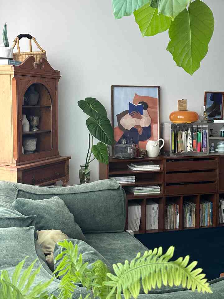 ナチュラルな色調のリビング、グリーンソファとヴィンテージ木製家具、本棚と植物が配置された雰囲気のある空間