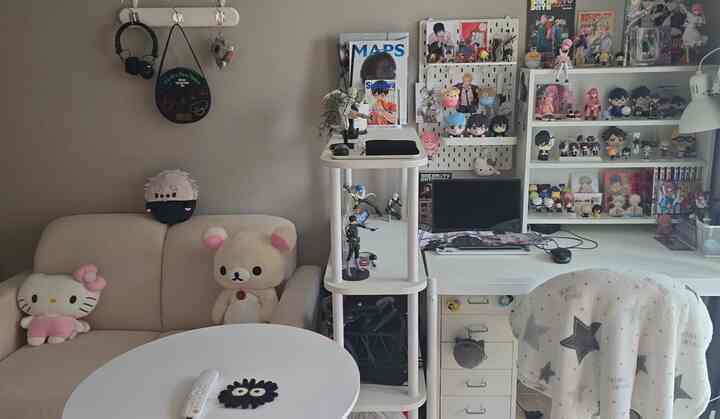 ホワイトとベージュのトーンが調和したコンパクトなオタク部屋。ソファ、デスク、多様な棚とアニメグッズが配置された整った空間。