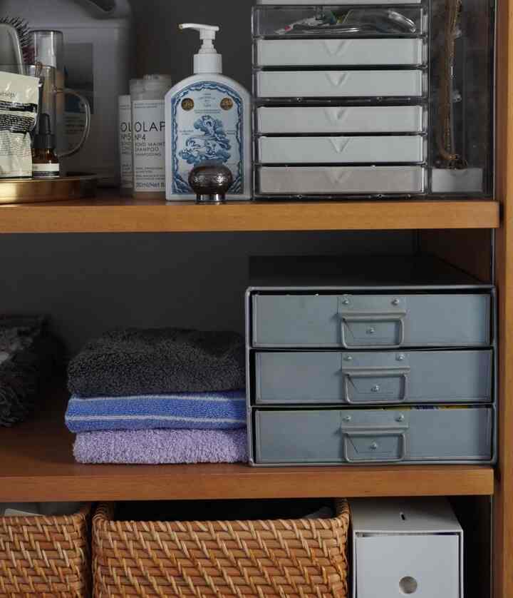 ナチュラルな色調の脱衣所の棚に、折りたたまれたタオルと様々な収納容器が整然と配置された雰囲気のあるインテリア