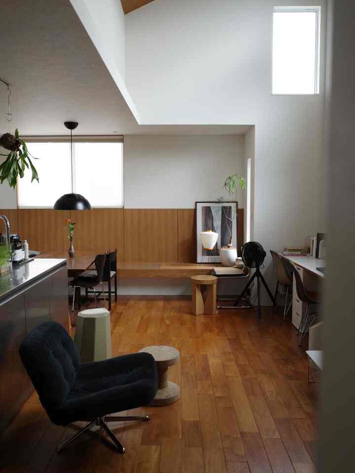 白い壁と木目調の床と家具が調和した2階リビング、スツールとダイニングテーブルが配置された自然な雰囲気のある印象的な空間