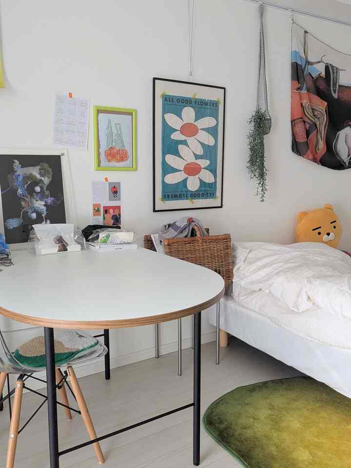 白と緑のトーンの寝室、白いテーブルとベッド、壁にポスターや布製品が配置されたシンプルで落ち着いた雰囲気のインテリア