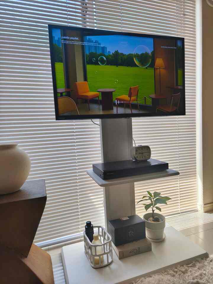 白とナチュラルカラーのリビングルーム、テレビ、フロアランプ、植物が配置されたモダンな雰囲気の空間