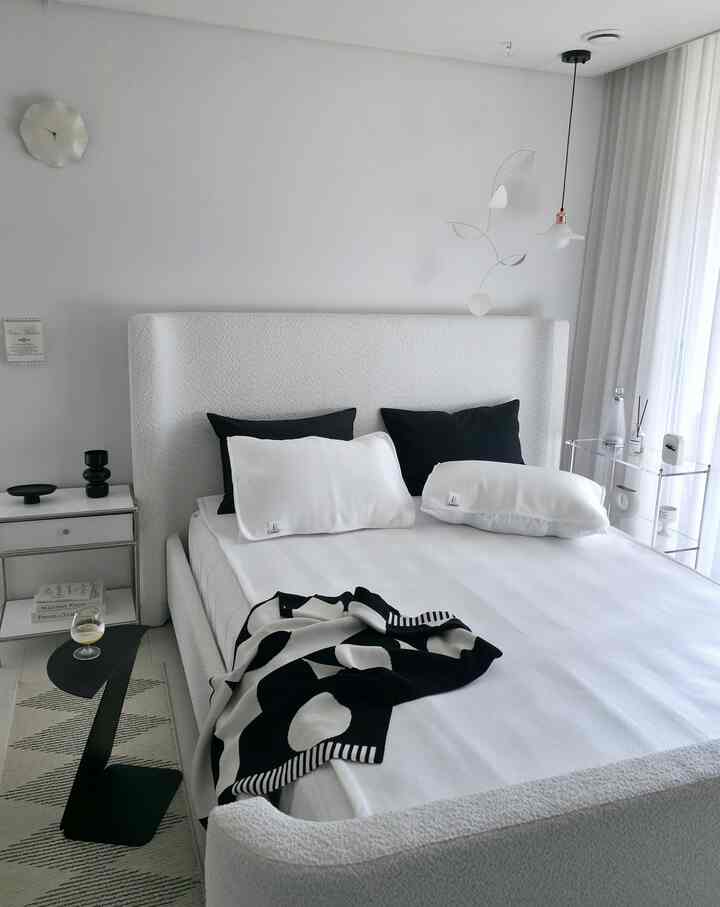 ホワイトとブラックのモノトーンでまとめられたモダンな寝室、ファブリックベッドとシンプルな寝具が配置された清潔感のある印象的な空間