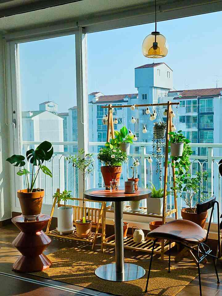 温かみのある木目調とブラウンが調和するバルコニー、豊富な植物と円形テーブルが置かれた雰囲気のあるガーデニングスペース