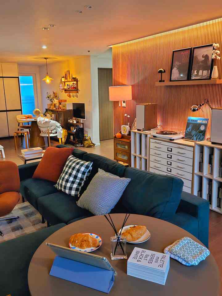 ネイビーソファとオレンジのアームチェアがあるナチュラルブラウンのリビング、壁のデコレーションと白い本棚が調和した落ち着いた空間