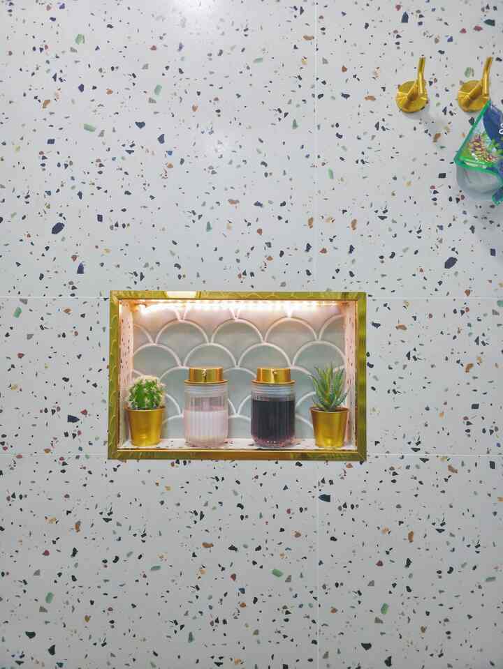 Bathroom wall with white terrazzo featuring colorful chips, gold-framed niche holding plants and gold containers, stylish and clean atmosphere
