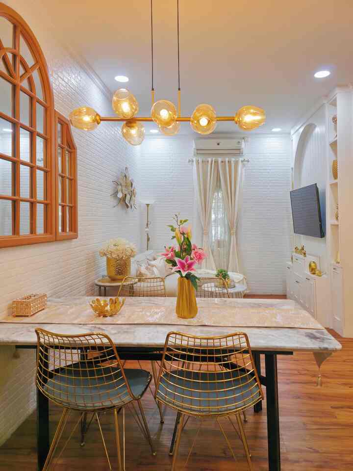 A contemporary living and dining room in gold and white tones, featuring metallic chairs and distinctive pendant lighting