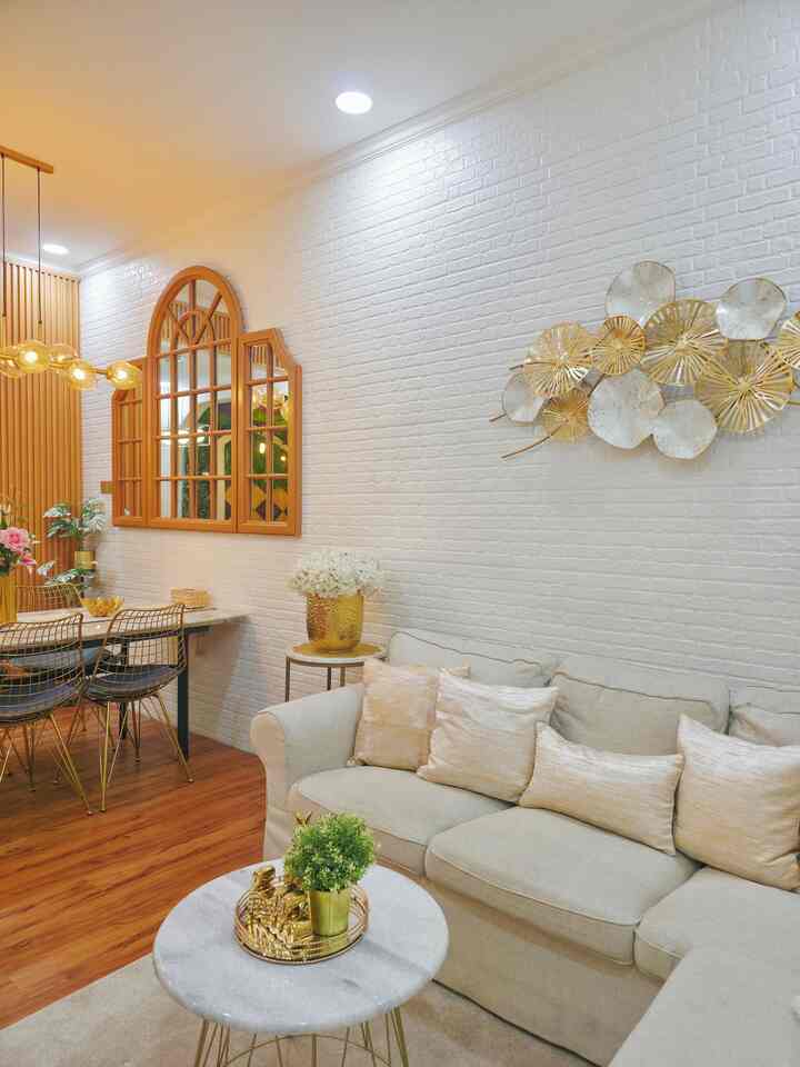 Bright white brick wall living room with natural modern tones, beige sofa, gold decor accents creating elegant atmosphere