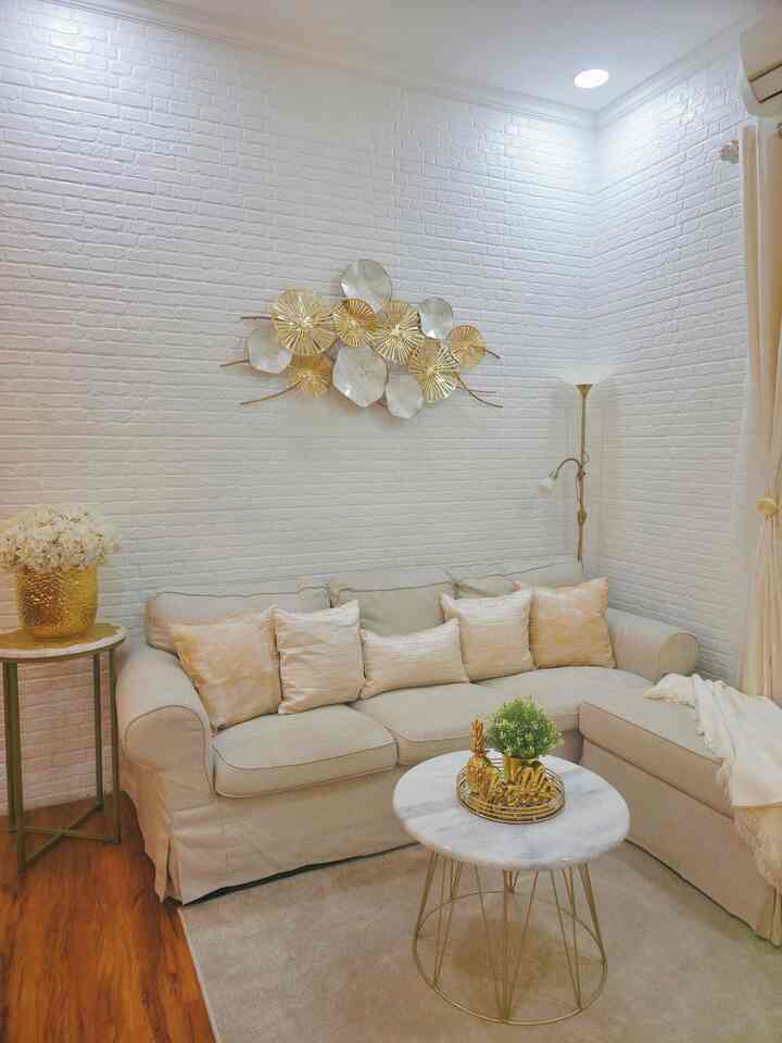 Cozy living room with white brick walls, beige corner sofa, and gold accents creating a harmonious atmosphere