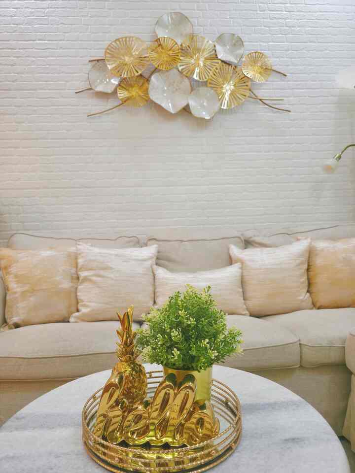 Gold and white toned living room featuring natural beige sofa with cushions, wall decor, and table decor in harmonious arrangement