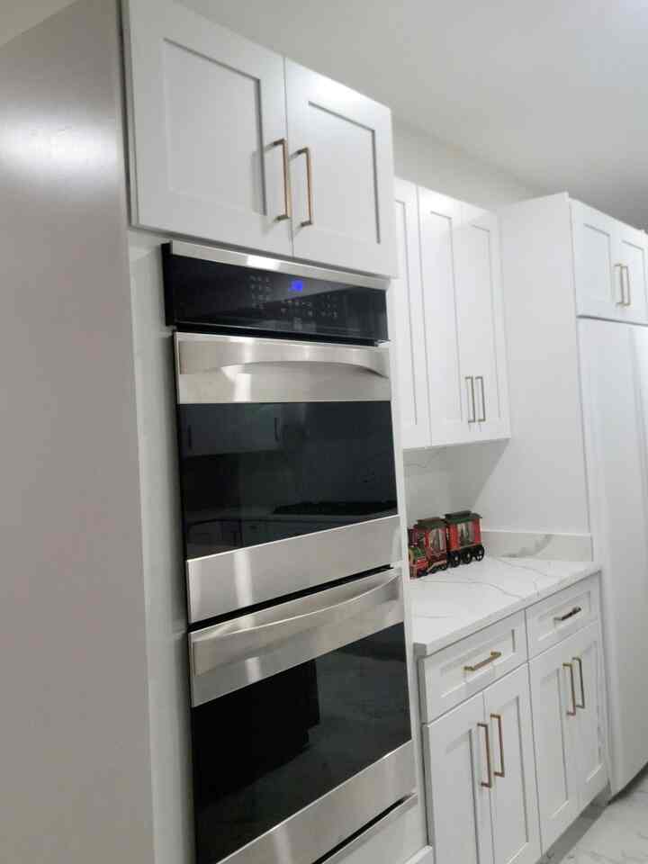 White-toned kitchen space featuring cabinets with gold handles and stainless steel ovens in a clean, modern setting