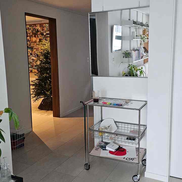 ホワイトとシルバーの色調のリビング入口空間、メタルトロリーと大きな壁面鏡が配置された清潔感あるインテリア