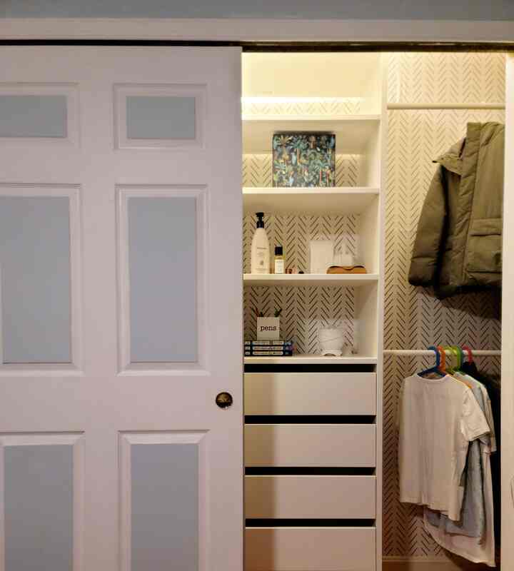 White-toned small closet featuring geometric patterned wallpaper, sliding door, and crisp storage drawers with a tidy interior