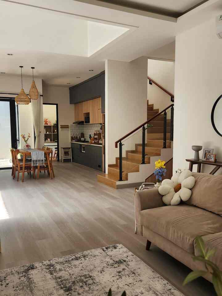 Light gray flooring and wood tone furniture harmonize in an open space living room and kitchen with a natural atmosphere