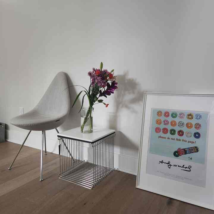 Entrance space with natural colors featuring an armchair, wire cube side table with vase, and a framed poster creating a simple clean interior