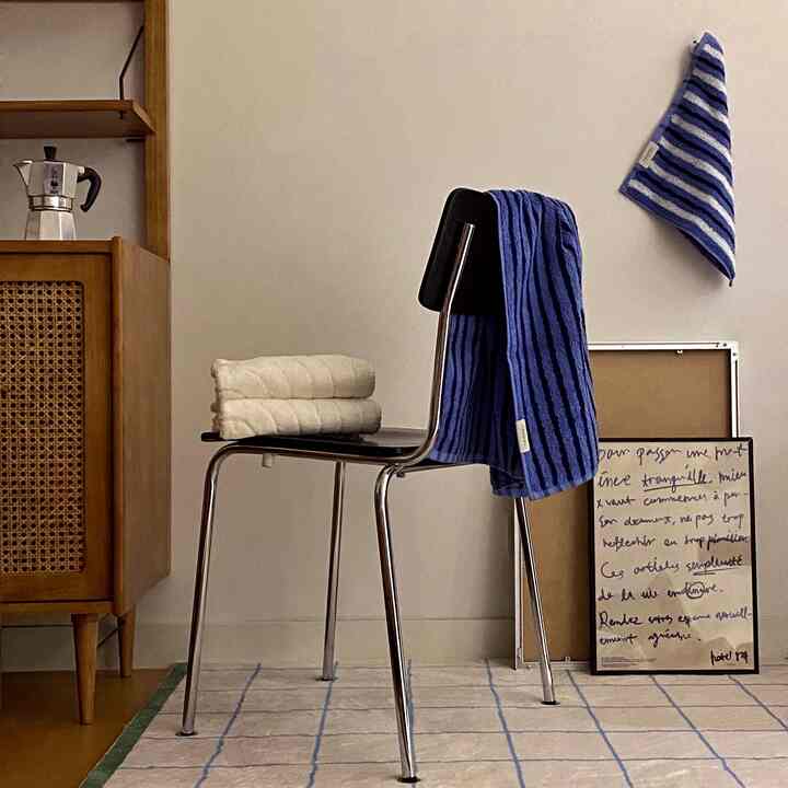 Natural-toned bathroom space featuring a black stool with blue and white towels neatly arranged, conveying a clean interior