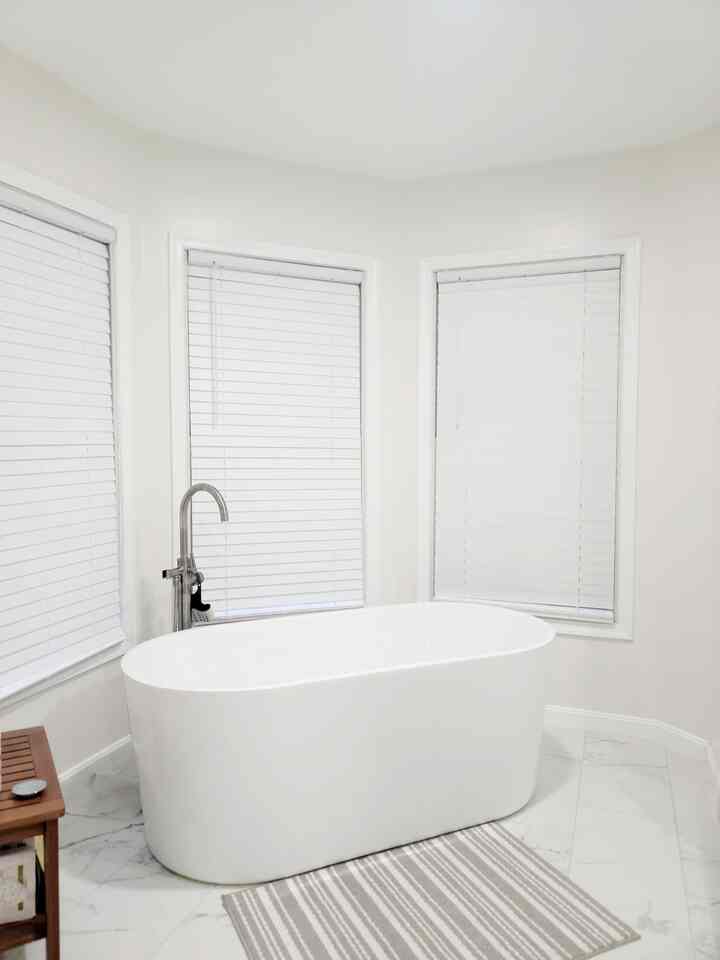 Natural toned bathroom featuring a central freestanding bathtub and a teak bench on the left with a simple, cozy atmosphere