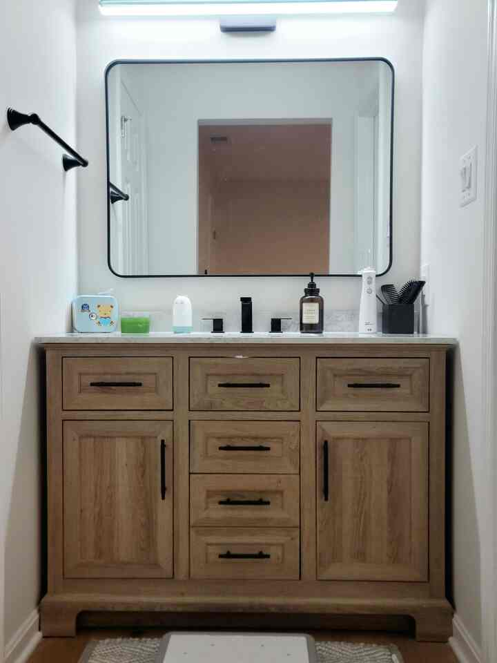 Natural wood tone vanity with black framed mirror in a small modern bathroom space