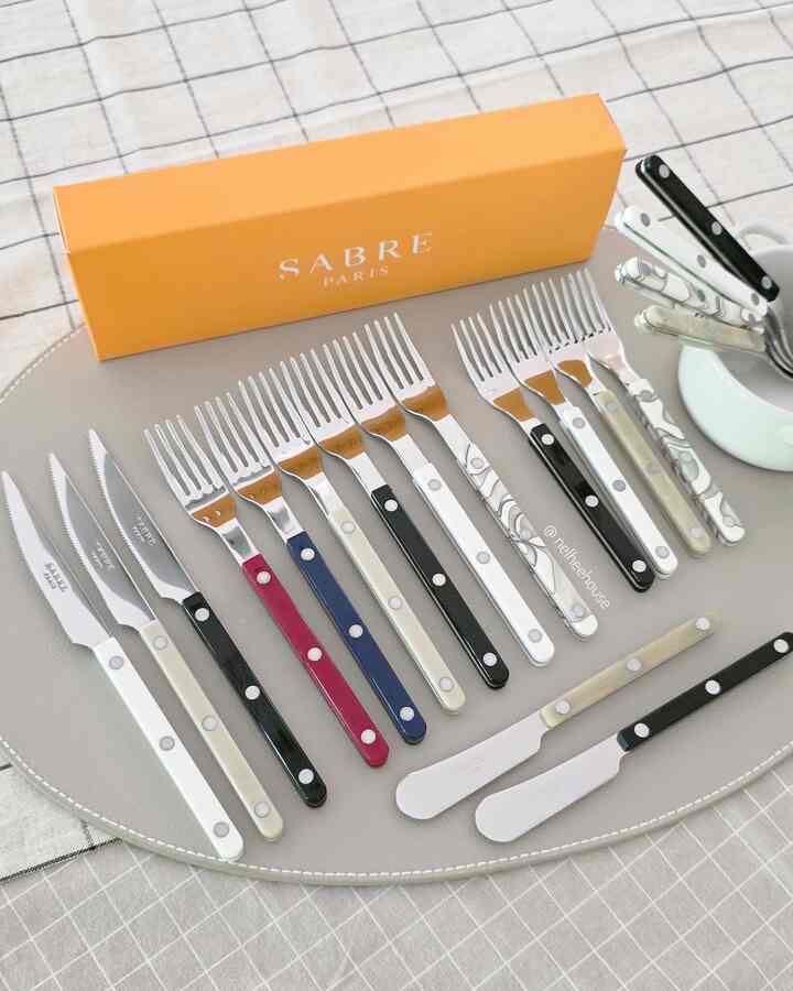 Kitchen cutlery with white and colorful handles arranged on a checkered tablecloth