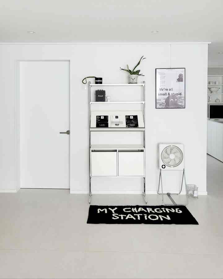 白と黒の配色のリビング、金属製の棚と黒い文字のラグが配置されたシンプルでモダンなインテリア