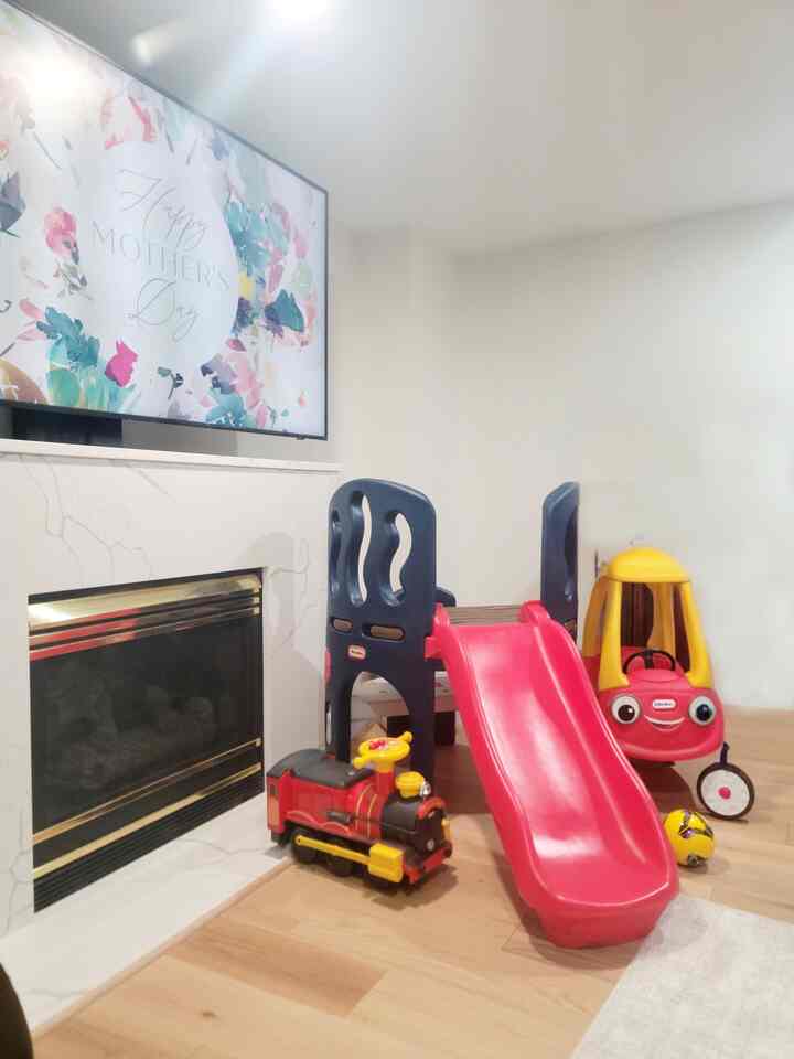 Bright kids' room with white walls and wood tone flooring, featuring a red slide and children's toys for a playful atmosphere