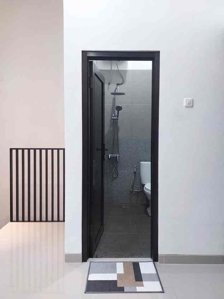 White and gray toned bathroom with a black door centered, featuring a modern geometric rug in front creating a clean space