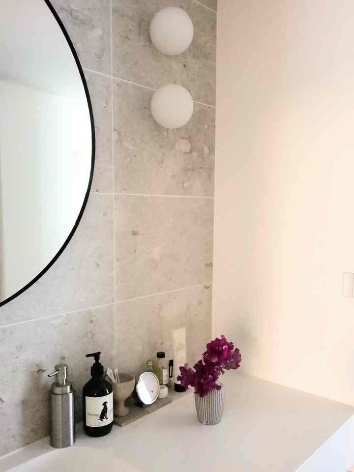 White and gray toned bathroom vanity with a round mirror and purple flowers, presenting a simple modern space