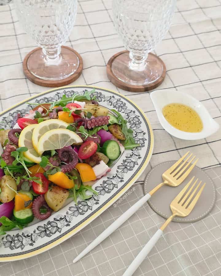 Home cafe style dining table with patterned tablecloth, gold-handled forks, and a serving dish filled with assorted vegetables
