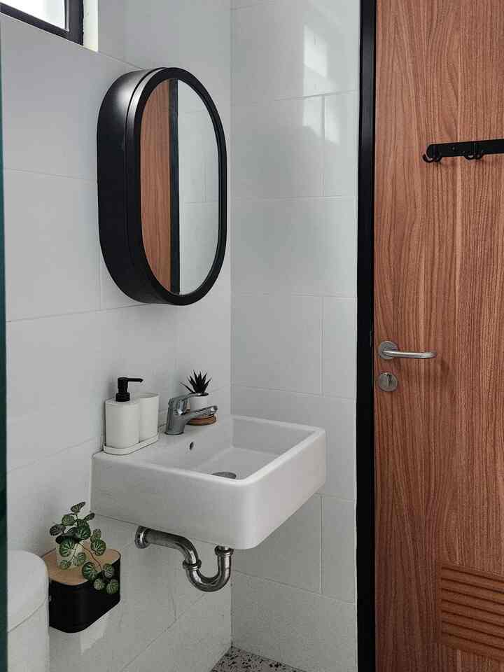 A white and natural color bathroom featuring a wash basin and oval black-framed mirror with a simple atmosphere