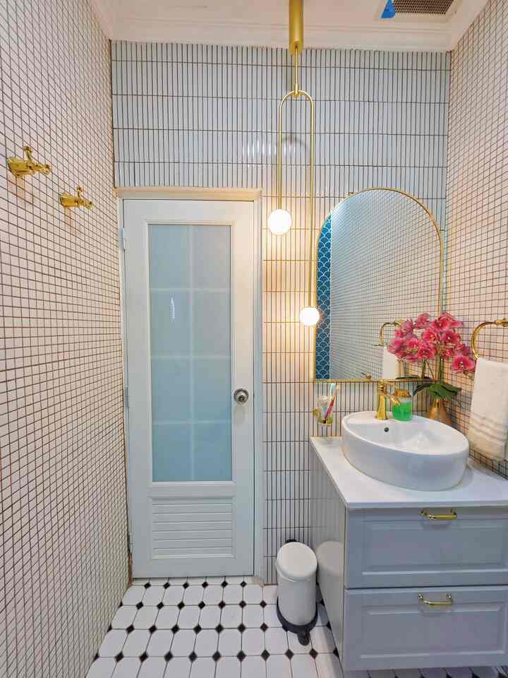 White and gold toned bathroom featuring a sink, arched mirror, plant, and elegant lighting creating a clean atmosphere