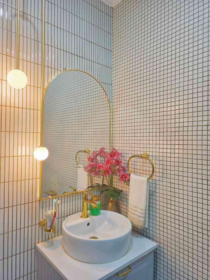 Bathroom with white tiled walls, featuring a gold arched mirror and white sink creating a luxurious atmosphere