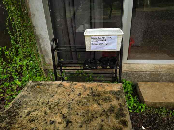 Outdoor entrance area featuring a black metal shoe rack with a white basket on top, natural stone flooring, and greenery nearby