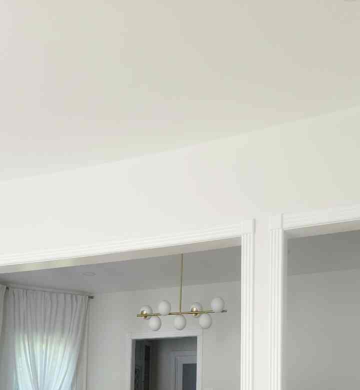 A simple modern space featuring white and gold ceiling and chandelier, with sheer curtains allowing natural light creating a clean interior