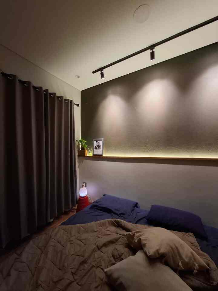 Cozy small bedroom with navy bedding and beige bedspread, softly lit by lamps and track lighting