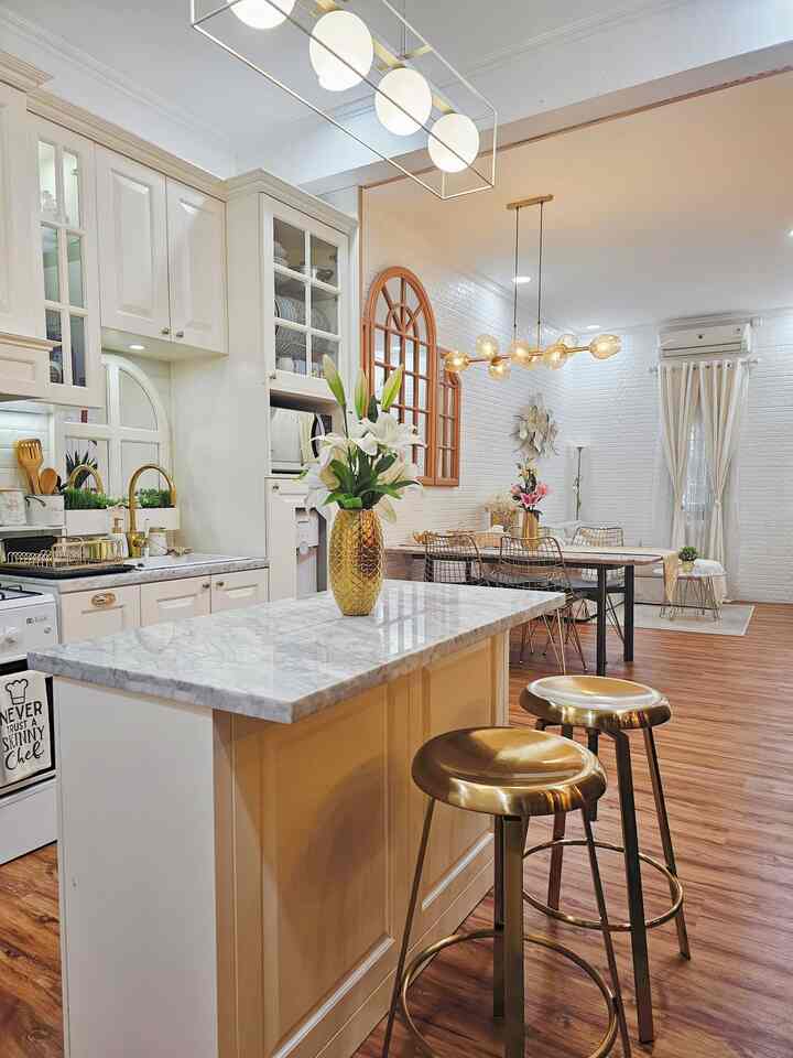 White and brown toned dining room and kitchen featuring gold accent bar stools and vase, creating an elegant atmosphere