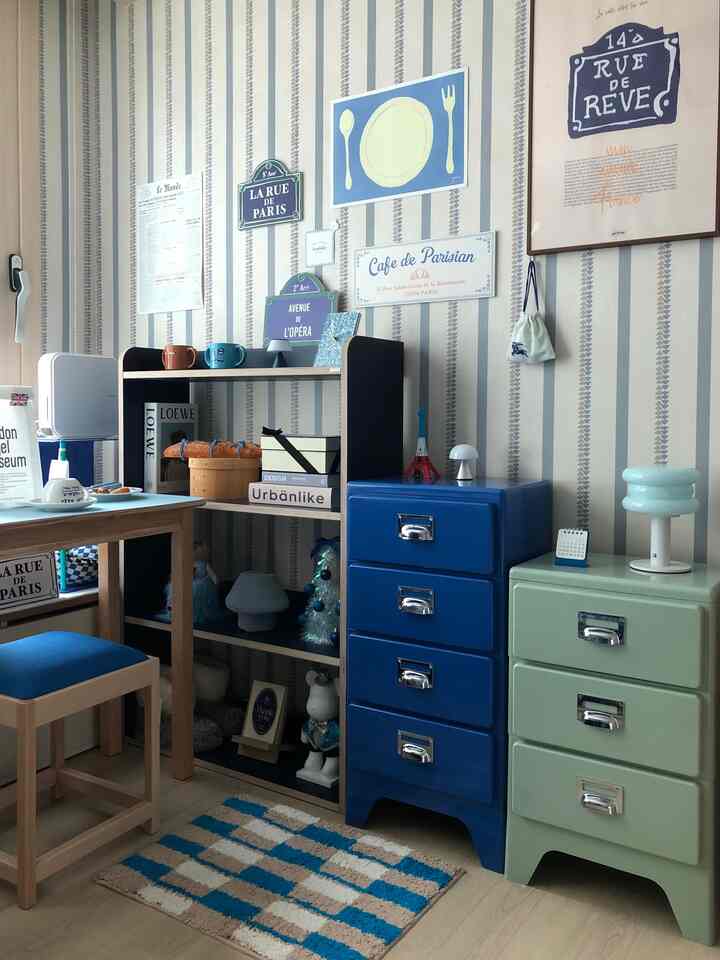 ベージュと青のトーンの落ち着いたダイニングルーム、木製テーブルと収納家具、カフェ風ポスターが配置された雰囲気のあるインテリア