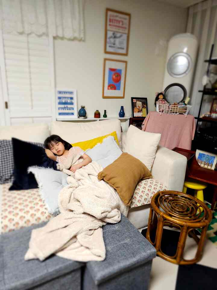 白と茶色のトーンのリビング、ヴィンテージソファとクッションの上で子供が安らかに眠る雰囲気のあるインテリア