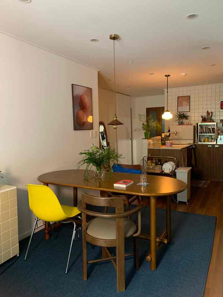 自然な木目調とブルーのラグが調和したリビングキッチンスペース、黄色のダイニングチェアとペンダントライトが配置された温かみのある雰囲気のインテリア