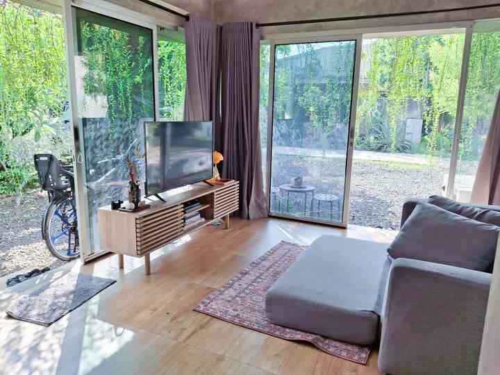Living room with transparent glass walls, wood tone flooring, and gray sofa bed, creating a cozy and spacious atmosphere