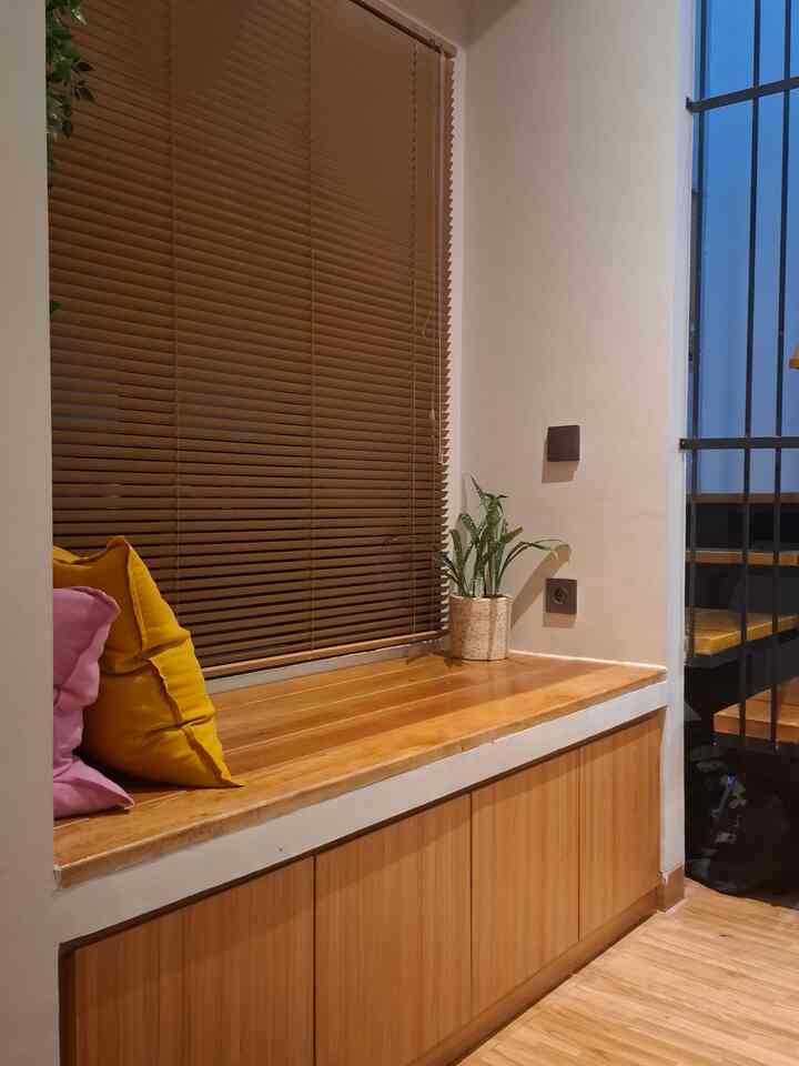 Cozy entrance area featuring warm wood tone bench and brown blinds, accented with a potted plant