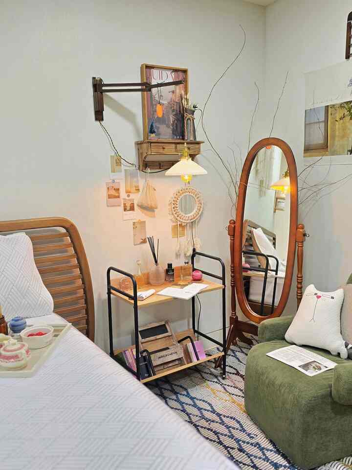 Natural-toned bedroom featuring wooden framed art, a full-length mirror, and a movable trolley shelf creating a cozy warm atmosphere