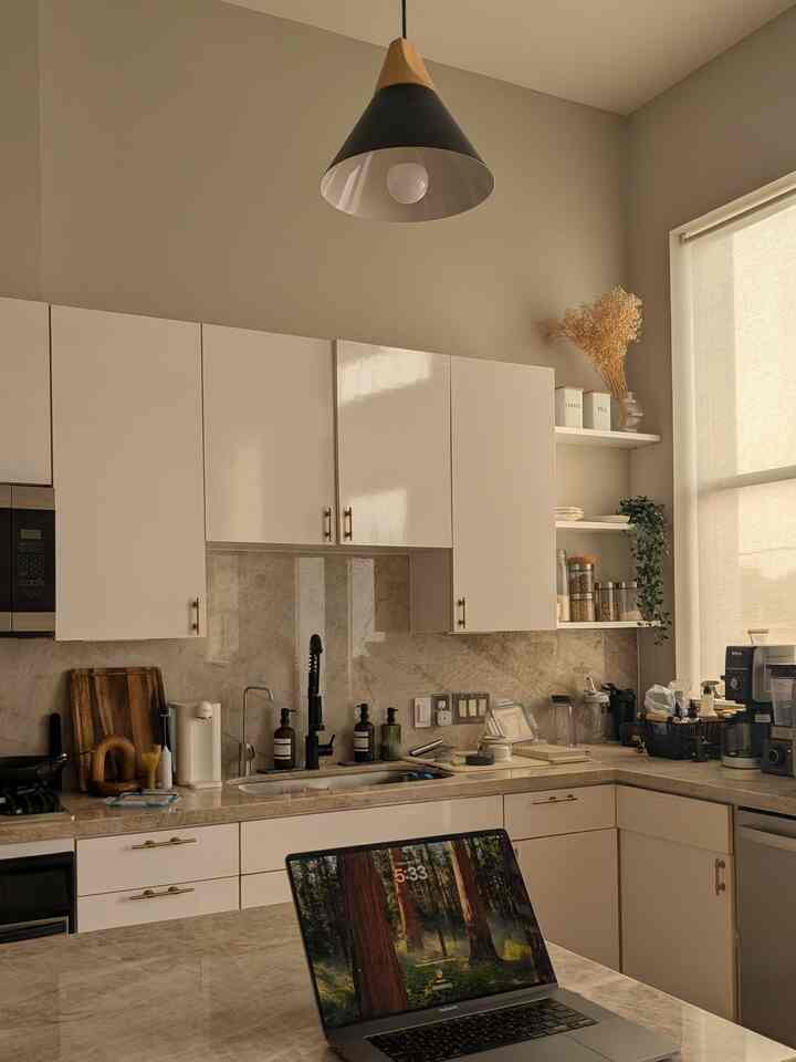 Warm beige and white toned kitchen featuring a central laptop and pendant light, creating a cozy and productive home office cafe atmosphere