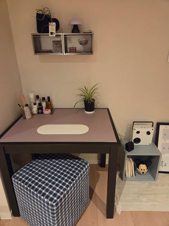 ナチュラルカラーの壁とウッドトーンの床がある寝室前の小さなスペースにチェック柄スツールとステンレス棚、植物が配置されたモダンなテーブル