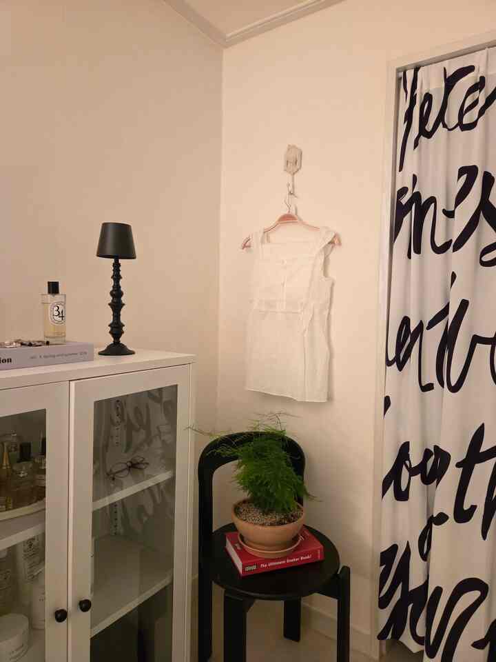 Ivory-toned bedroom corner with white cabinet and black chair topped with green plant creating cozy atmosphere