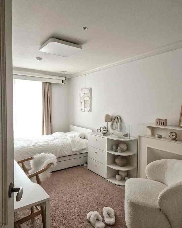 白とナチュラルトーンの小さな寝室、ベッド、ナイトテーブル、アームチェア、机が配置された雰囲気のあるインテリア