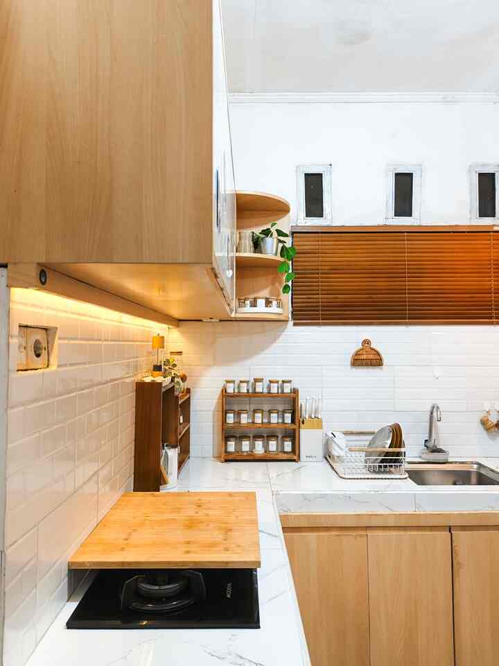 Cozy kitchen with wood tones and white tiles, featuring wooden blinds and neatly organized storage items