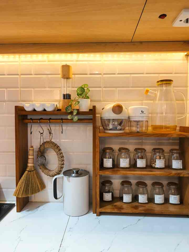Cozy kitchen space featuring natural brown wood shelves with white tiled wall, displaying various kitchen utensils and storage items