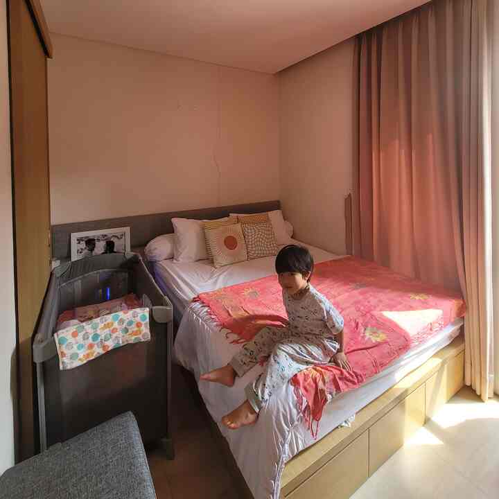 Natural beige tone bedroom featuring a bed with pink blanket, pillows, and a child sitting comfortably